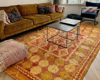 Puede incluir: Un salón con un sofá de terciopelo color mostaza, cojines decorativos y una alfombra con diseños en tonos rojos, amarillos y naranjas. Dos mesas de centro cuadradas negras sobre la alfombra. Un sillón azul en el fondo.