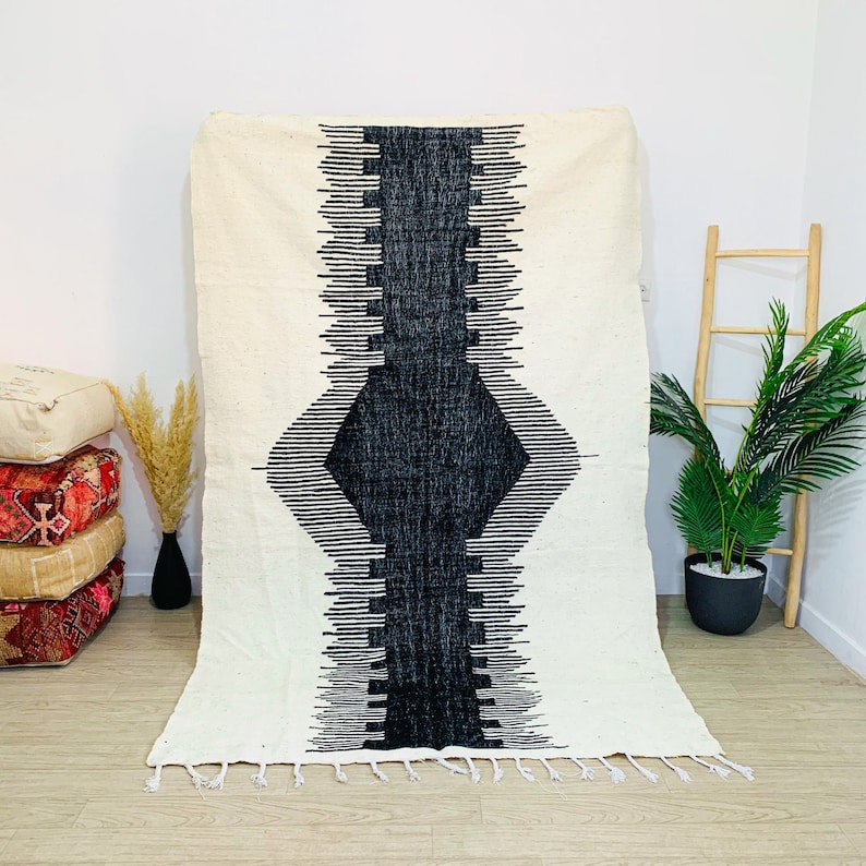 May include: A black and white geometric patterned rug with fringe on the bottom edge. The rug is on a wooden floor.