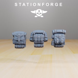 May include: Three gray backpacks with skull and crossbones emblems. Each pack features multiple compartments, straps, and buckles. The word "STATIONFORGE" is printed above the backpacks, along with a skull logo.