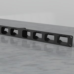 Puede incluir: Sistema de gestión de cables de metal negro con ocho ranuras para organizar cables y alambres. El sistema está diseñado para montarse en una pared o un escritorio.