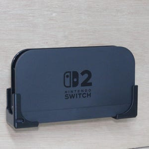 May include: A dark blue Nintendo Switch dock, featuring the Nintendo Switch logo and the number 2. It's mounted on a light wooden surface with a black holder. The dock is designed for the Nintendo Switch console.