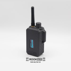 May include: A black handheld radio transmitter with a small antenna and a blue digital display. The radio has a textured surface and the text "ROOK PRO FOR HELTEC V3" is printed on the bottom.