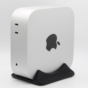 May include: A silver Mac mini computer with a black stand. The computer has a black Apple logo on the front.