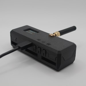 May include: A black, rectangular device with a small screen, a USB-C port, and a black antenna. The device has the word "FGR" printed on it.