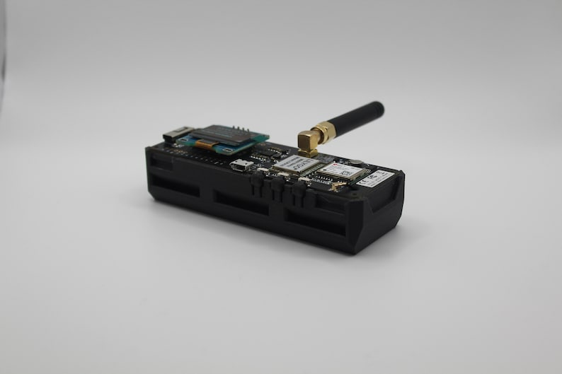May include: A black electronic device with a small antenna, a circuit board, and a small screen. The device is on a white surface.