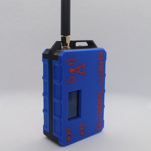 May include: A blue and black device with a small screen and a red button. The device has a black antenna and the text "GLOBAL LORA" printed on the side.