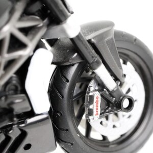 May include: Close-up of a black and silver motorcycle model. The front wheel and brake system are visible, with the word "brembo" on the brake caliper. The tire has a detailed tread pattern.