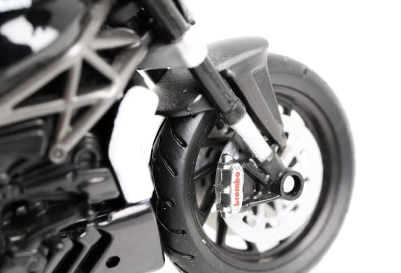 May include: Close-up of a black and silver motorcycle model. The front wheel and brake system are visible, with the word "brembo" on the brake caliper. The tire has a detailed tread pattern.