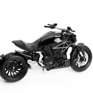 May include: A black Ducati motorcycle model with a glossy finish. The model features detailed components, including the engine, wheels, and seat. The word "Ducati" is visible on the fuel tank. The motorcycle is set against a white background.