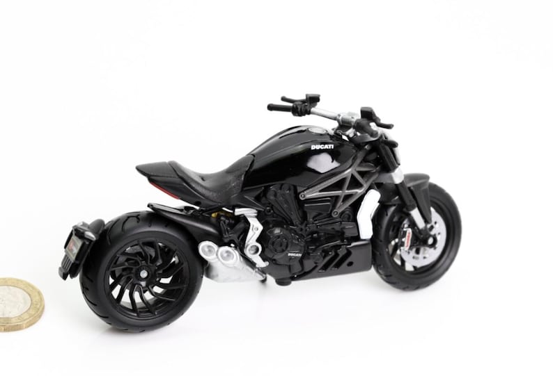 May include: A black Ducati motorcycle model with a glossy finish. The model features detailed components, including the engine, wheels, and seat. The word "Ducati" is visible on the fuel tank. The motorcycle is set against a white background.