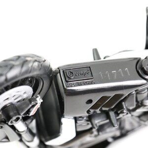 May include: A black and white toy motorcycle with a detailed design. The motorcycle has a visible tire, brake disc, and the text "11711". The brand "Burago" and "Made in China" are also visible.