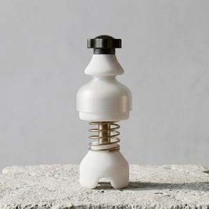 Peut inclure: Un moulin à sel ou à poivre blanc et noir avec un ressort de couleur laiton. Le moulin a un design unique avec une base arrondie et un dessus noir. Il est posé sur une surface grise texturée.