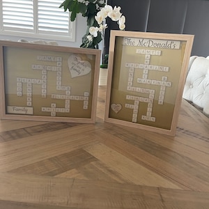 May include: Two framed wooden scrabble tile word art pieces. The first piece says "The McDonald's" and includes the names James, Katharine, Makynan, Alisha, Teagan, and Ken. The second piece says "Together we are a family" and includes the names James, Archie, Teagan, Don, Rob, Elliarna, Kristy, and Family.