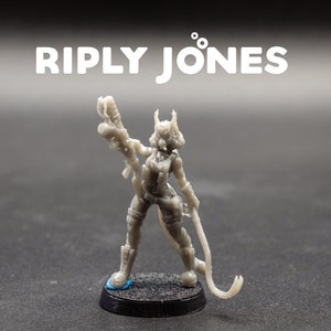 May include: A gray miniature figurine of a female character, holding a weapon and a whip. The figurine is on a black base with the text "RIPLY JONES" in white above it. The character is wearing a futuristic outfit.