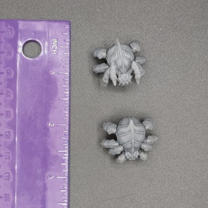 Może przedstawiać: Dwie szare plastikowe figurki pająk&oacute;w, każda z ośmioma nogami i segmentowanym ciałem. Pająki mają około 2,5 cm wysokości.