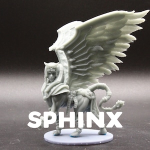 May include: A gray 3D printed figurine of a sphinx with wings. The sphinx has a human head with a crown and a lion's body with a tail. The figurine is standing on a round base.