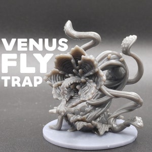 May include: A gray 3D printed miniature of a Venus flytrap with a textured surface and intricate details. The plant is depicted with its mouth open, revealing sharp teeth. The miniature is set on a gray base.