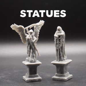 May include: Two gray statues of figures in hooded robes, one with wings and a scythe, the other with a sword. Both statues are on square bases.