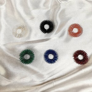 May include: Six acupressure rings in different colours, including white, black, red, green, blue, and maroon. The rings are made of plastic and have small spikes on the outside.