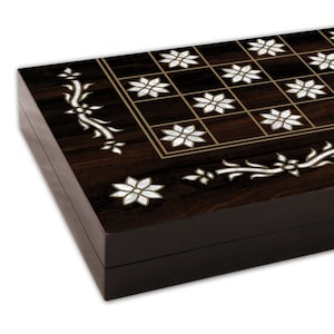 May include: A dark brown wooden game board with a checkerboard pattern inlaid with white mother-of-pearl flowers. The board has a decorative border of floral designs.