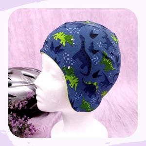 Könnte beinhalten: Blau-grüner Fleece-gefütterter Beanie mit Dinosaurier-Druck. Die Mütze hat ein grünes Fleece-Futter und eine blaue Außenseite mit einem Dinosaurier-Druck.