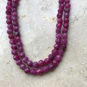 Puede incluir: Un collar de doble cadena hecho de cuentas de rubí facetadas. Las cuentas son de un color rojo intenso y rico y están enhebradas en un cordón transparente.