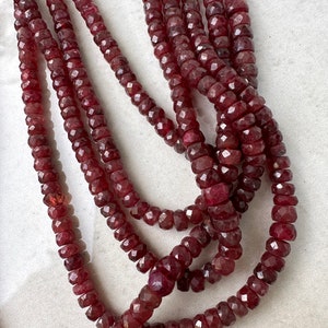 Może przedstawiać: Szereg ciemnoczerwonych koralików rubinowych, fasetowanych i nawleczonych. Koraliki są małe i jednolite, tworząc gładki i elegancki wygląd.