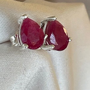 Könnte beinhalten: Ein Paar silberne Ohrringe mit birnenförmigen roten Rubin-Edelsteinen.
