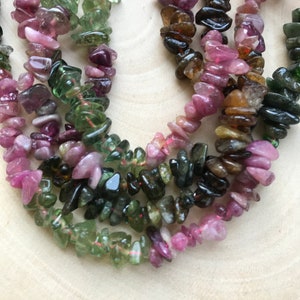 Può includere: Un filo di schegge di pietre preziose multicolori, tra cui rosa, verde e marrone, infilate su un filo trasparente. Le schegge sono di forma irregolare e hanno una finitura naturale e lucida.