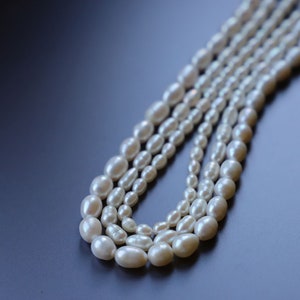 May include: A strand of white pearl beads, arranged in a layered pattern, on a dark blue background.