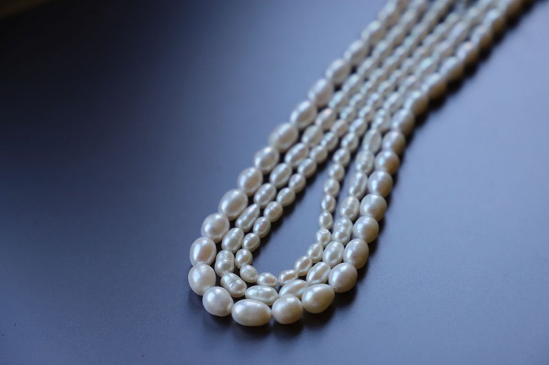 May include: A strand of white pearl beads, arranged in a layered pattern, on a dark blue background.