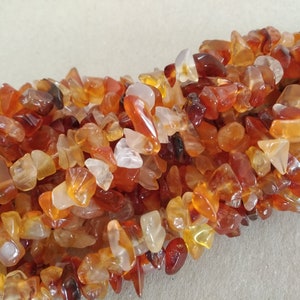 Op de afbeelding: Close-up van een stapel carneool edelsteen chips. De chips variëren in grootte en vorm en vertonen tinten oranje, rood en amber. Deze gepolijste stenen worden vaak gebruikt in sieraden en ambachten.