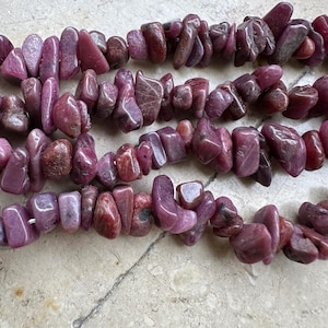 Op de afbeelding: Een streng roze en paarse edelsteen chips, met een ruwe, onregelmatige vorm. De chips zijn aan elkaar geregen op een doorzichtige draad.