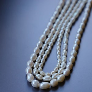 May include: A strand of white pearl beads, arranged in a layered, cascading pattern. The pearls are oval-shaped and have a smooth, lustrous finish.