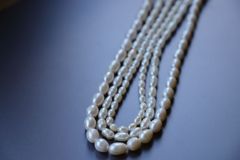 May include: A strand of white pearl beads, arranged in a layered, cascading pattern. The pearls are oval-shaped and have a smooth, lustrous finish.