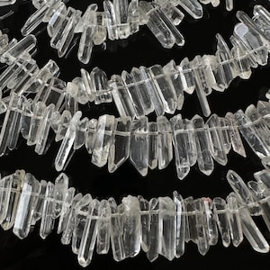 Pode incluir: Uma linha de pontas de cristal de quartzo transparente, também conhecido como cristal de rocha, dispostas em um padrão escalonado sobre um fundo preto. As pontas têm vários comprimentos e um acabamento natural e bruto.