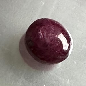 Könnte beinhalten: Ein tiefroter Edelstein mit einer glatten, abgerundeten Oberfläche. Der Edelstein ist oval geformt und hat einen leichten Glanz.