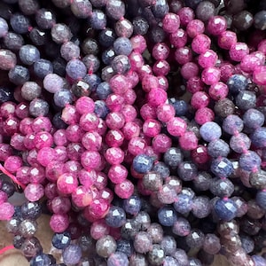 Könnte beinhalten: Nahaufnahme einer Sammlung facettierter Edelsteinperlen in Rosa-, Lila- und Grautönen. Die Perlen sind aufgefädelt und bilden eine strukturierte und farbenfrohe Darstellung. Die Perlen werden wahrscheinlich für die Schmuckherstellung verwendet.