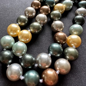 Può includere: Una collana multifilo realizzata con grandi perle rotonde finte in tonalità di verde, oro e crema.
