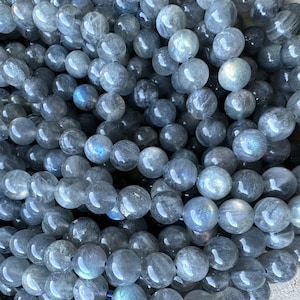 Peut inclure: Gros plan d'un brin de perles de labradorite grise. Les perles sont rondes et lisses, avec un léger éclat iridescent.