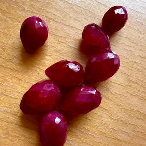 Op de afbeelding: Een verzameling gefacetteerde, druppelvormige robijn edelstenen. De dieprode stenen liggen op een lichtbruin houten oppervlak, vangen het licht en tonen hun facetten. Deze edelstenen zijn ideaal voor het maken van sieraden.