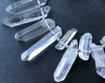 May include: A necklace made of clear quartz crystal points, connected by silver metal beads. The points are various lengths and are arranged in a cascading pattern.