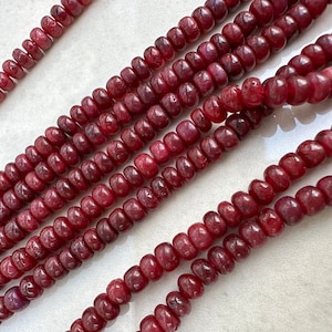 Może przedstawiać: Szereg ciemnoczerwonych koralików rubinowych, każdy koralik jest okrągły i lekko wydłużony, tworząc fakturowany wygląd. Koraliki są nawleczone na sznurek, tworząc długą naszyjnik.