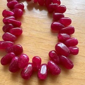 Könnte beinhalten: Eine Kette aus tiefrosa Edelsteinperlen, jede Perle hat eine Tropfenform mit einer glatten, polierten Oberfläche.
