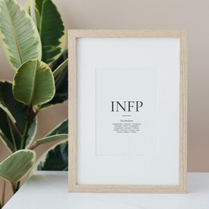 May include: A framed print with the letters INFP in a minimalist design. The print includes the words "The Mediator" and a list of associated traits. The frame is light-colored wood, and the background is white.