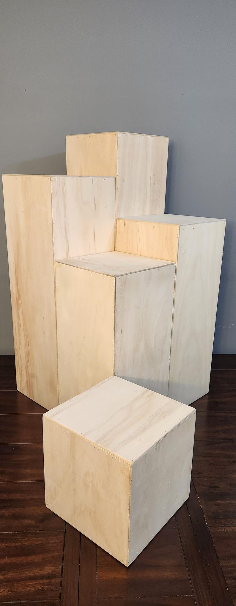 Puede incluir: Un conjunto de cuatro elevadores de exhibici&oacute;n de madera en varios tama&ntilde;os, hechos de madera de color claro con un acabado natural. Los elevadores est&aacute;n dispuestos en una formaci&oacute;n escalonada, creando una plataforma de exhibici&oacute;n en niveles.