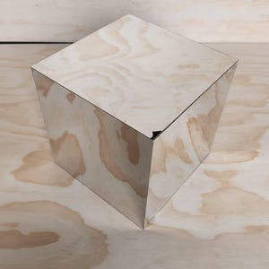 May include: A reflective, mirrored cube object with a smooth, polished surface. The cube features sharp, clean edges and corners, creating a geometric shape that reflects its surroundings. The surface is highly reflective, showing clear light.