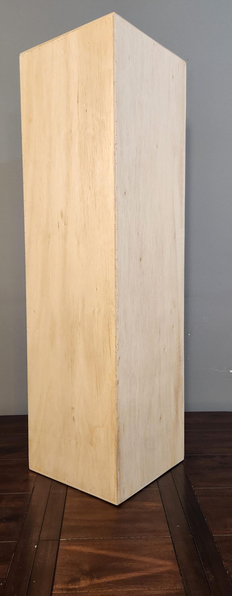 Puede incluir: Una caja de madera simple, de color marr&oacute;n claro, con una superficie lisa. La caja est&aacute; sentada en un suelo de madera marr&oacute;n oscuro.