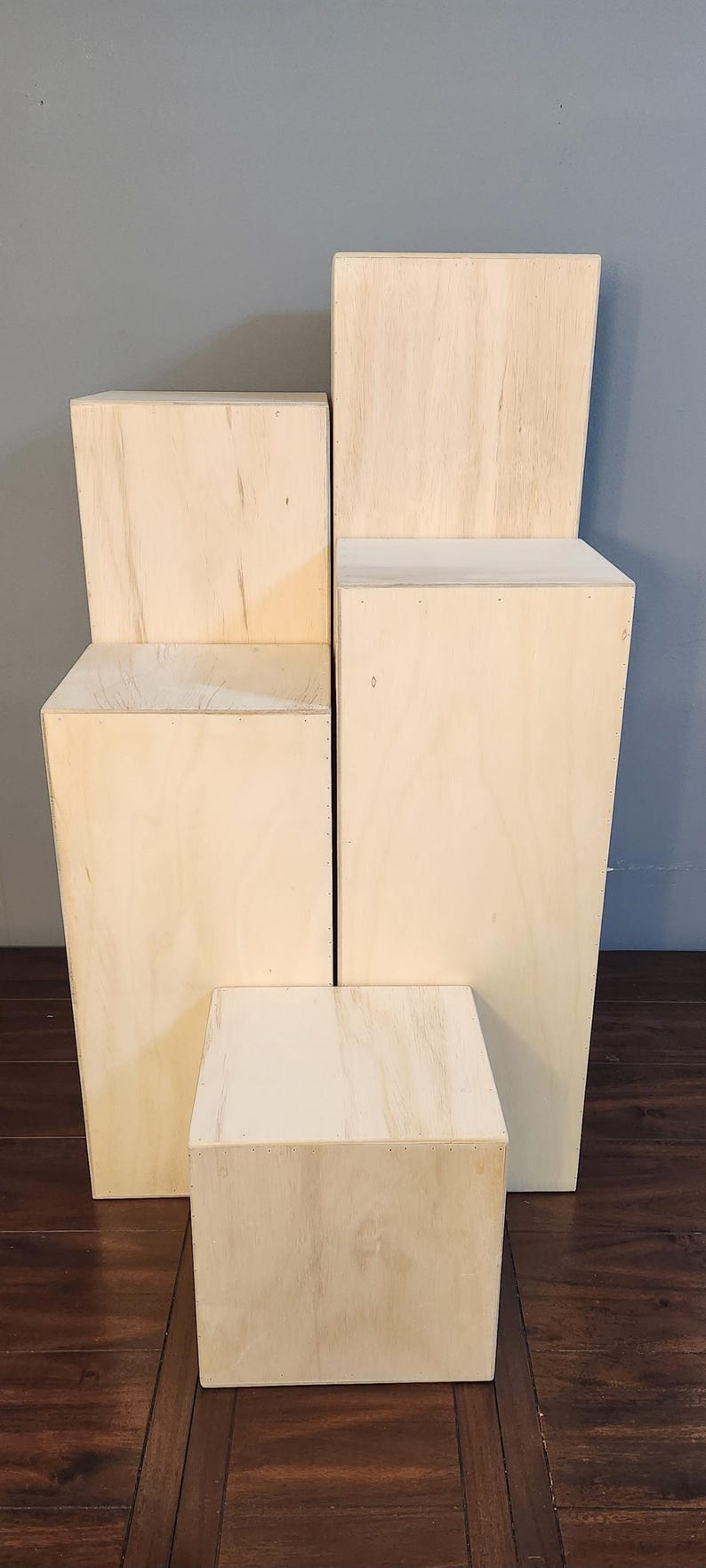 Puede incluir: Cuatro elevadores de exhibici&oacute;n de madera de diferentes tama&ntilde;os, apilados uno encima del otro. Los elevadores est&aacute;n hechos de madera de color claro y tienen una superficie lisa y sin terminar.