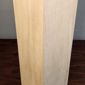 Puede incluir: Un pedestal rectangular de madera clara lisa con una superficie lisa. El pedestal est&aacute; sobre un suelo de madera oscura.